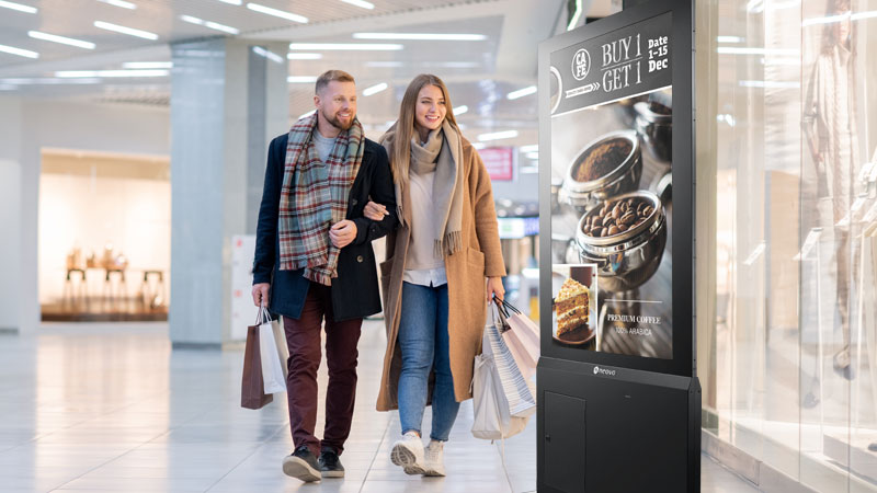 A couple is passing by digital signage in front of a retail store