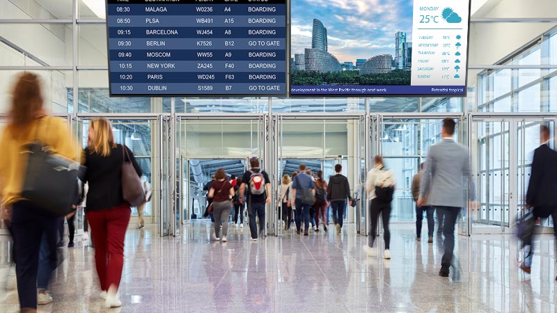 Two digital signage displays are mounted in the airport.