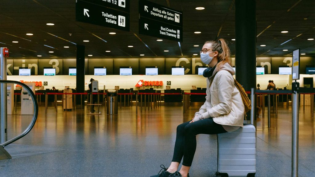 A woman wearing a mask sitting on her luggage at the airport during Covid-19 pandemic